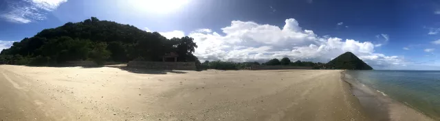 hier der Strand in einem Panorama Bild, der sich zwischen zwei Hügeln erstreckt und etwa 400m lang ist.